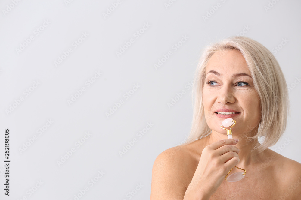 Mature woman with facial massage tool on light background