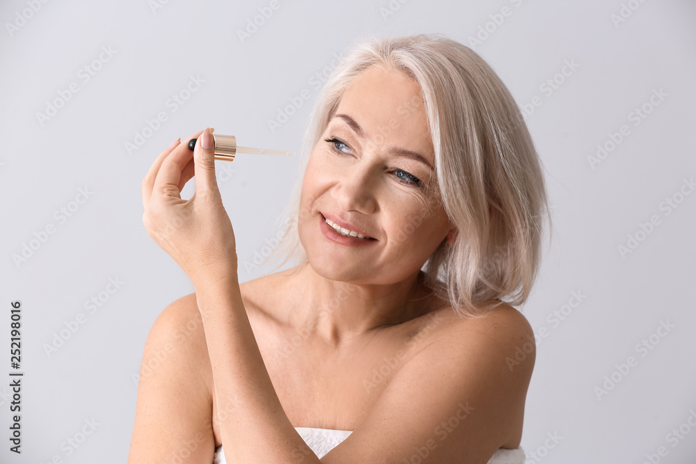 Mature woman applying face serum on light background