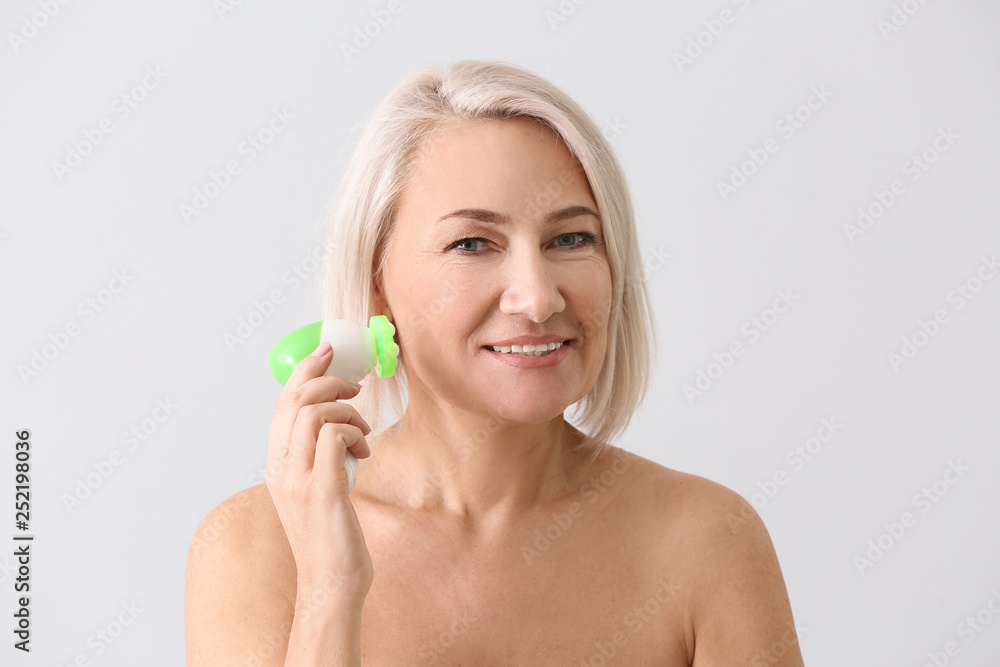 Mature woman with facial massage tool on light background