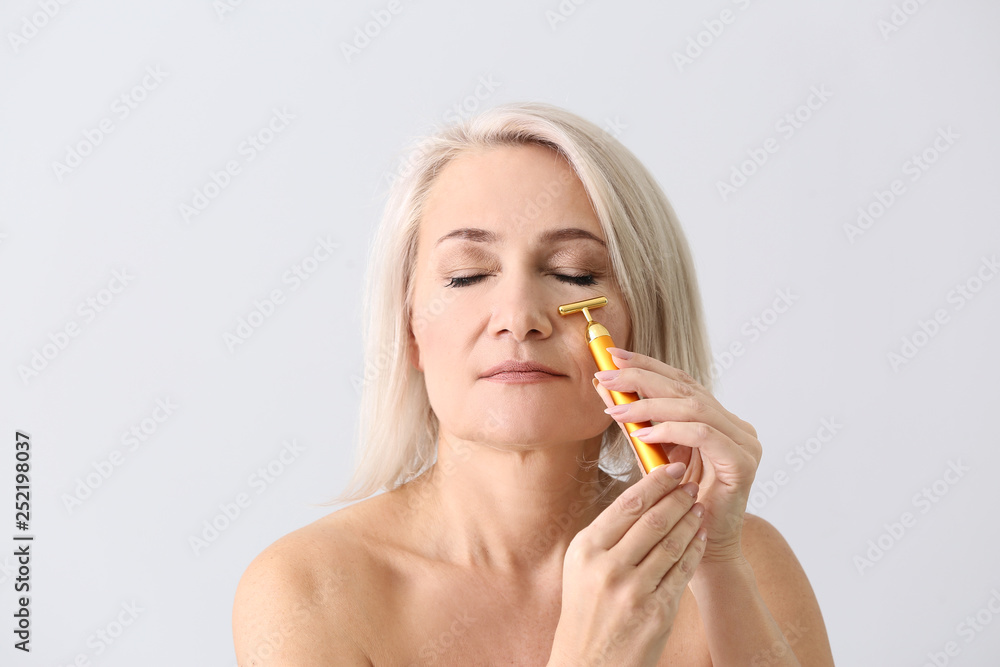 Mature woman with facial massage tool on light background