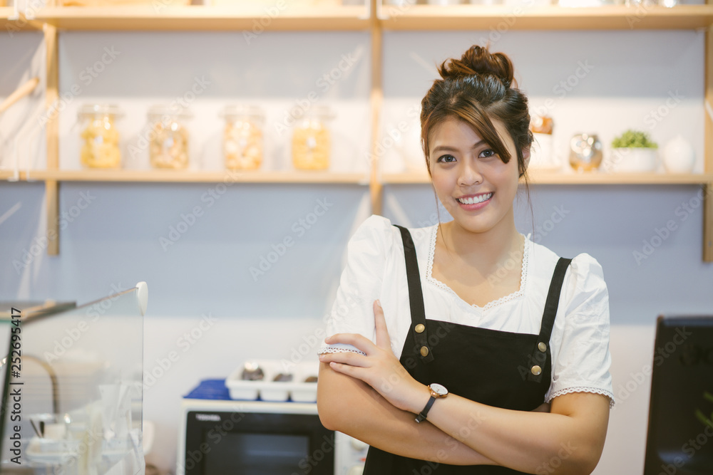 亚洲女服务员穿着围裙站在咖啡店里的肖像。