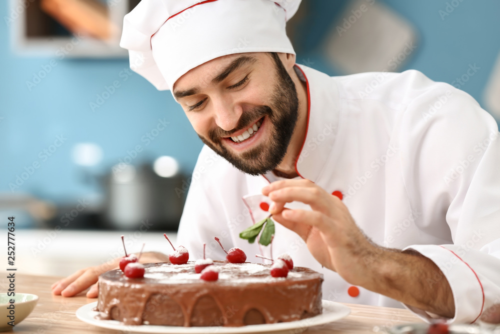 Male confectioner decorating tasty chocolate cake in kitchen