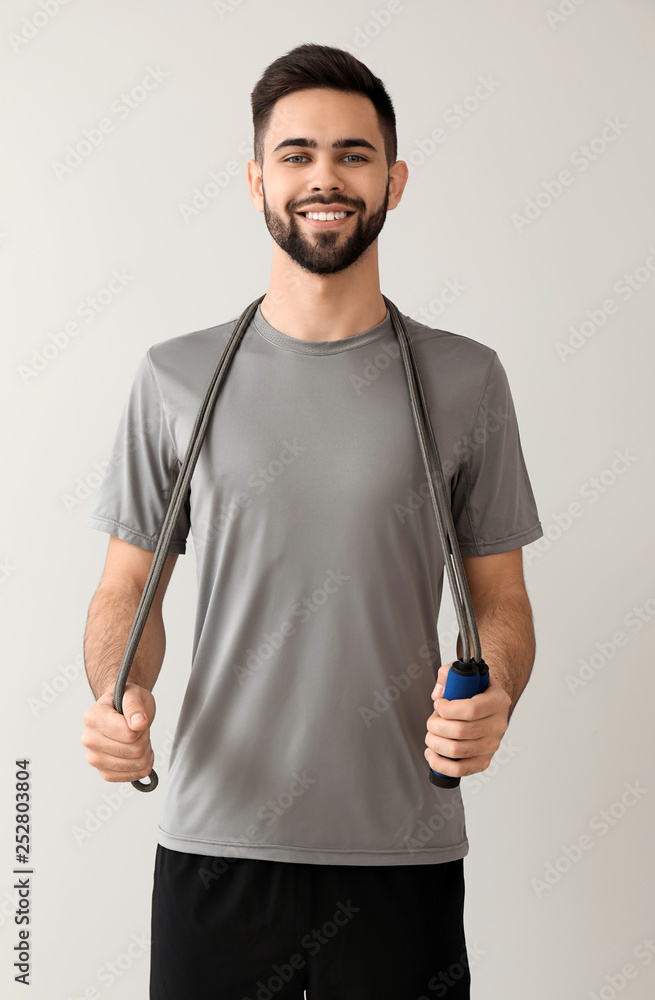 Sporty young man with jumping rope on light background