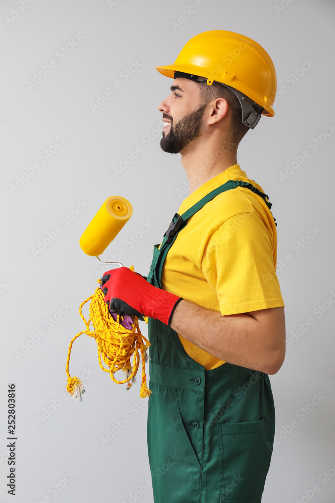 Worker with paint roller on light background