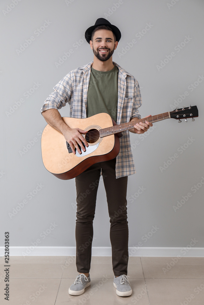 Handsome musician with guitar near light wall