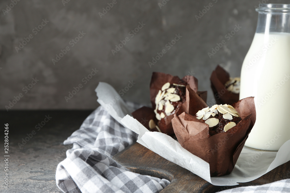 Board with tasty almond muffins and milk on grey table