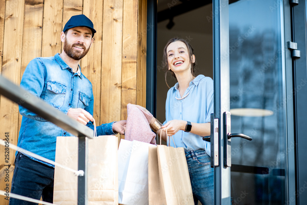 Delivery man bringing some goods packaged in paper bags for a young woman client to home. Buying clo