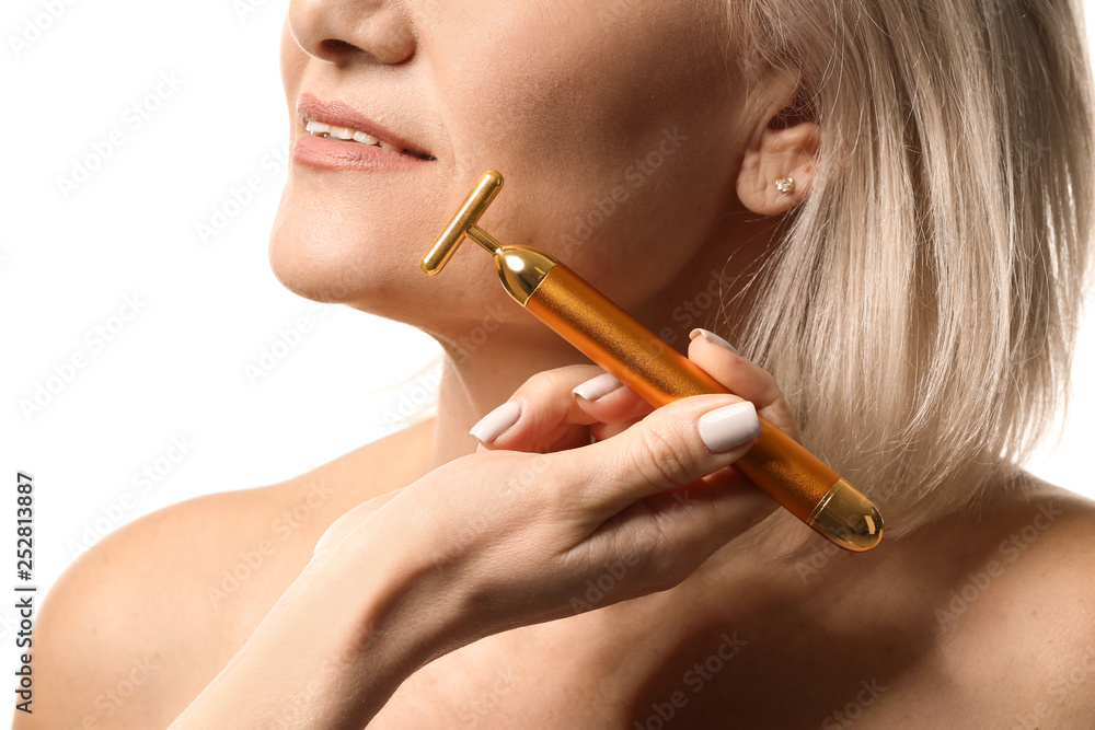 Mature woman with facial massage tool on white background, closeup