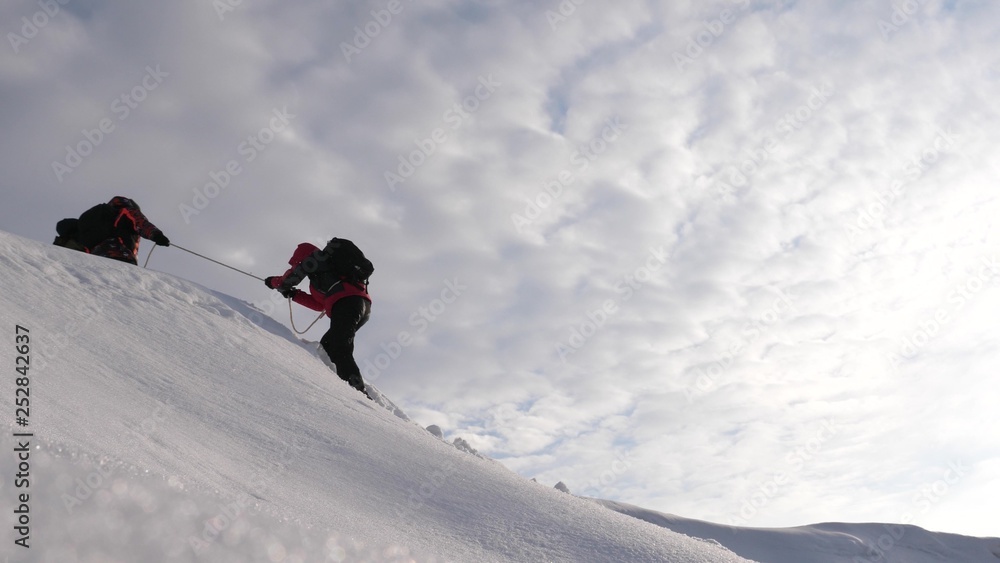 旅行者在大风中爬上绳索，穿过雪地上坡。冬季游客努力工作。