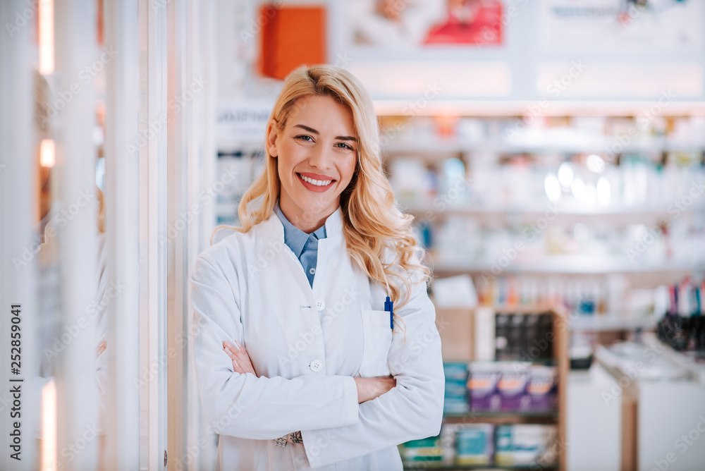 Portrait of a young smiling blonde druggist at work, looking at camera.