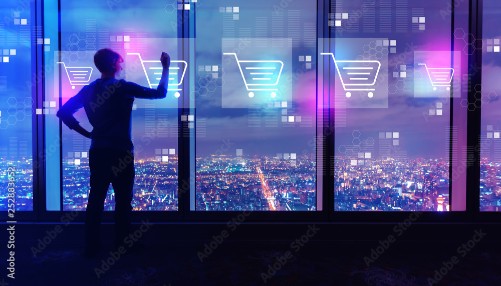 Online shopping theme with man writing on large windows high above a sprawling city at night