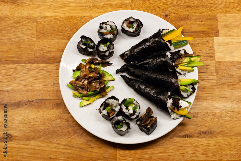 Homemade vegan Sushi rolls and temaki filled with avocado on a plate on a wooden table