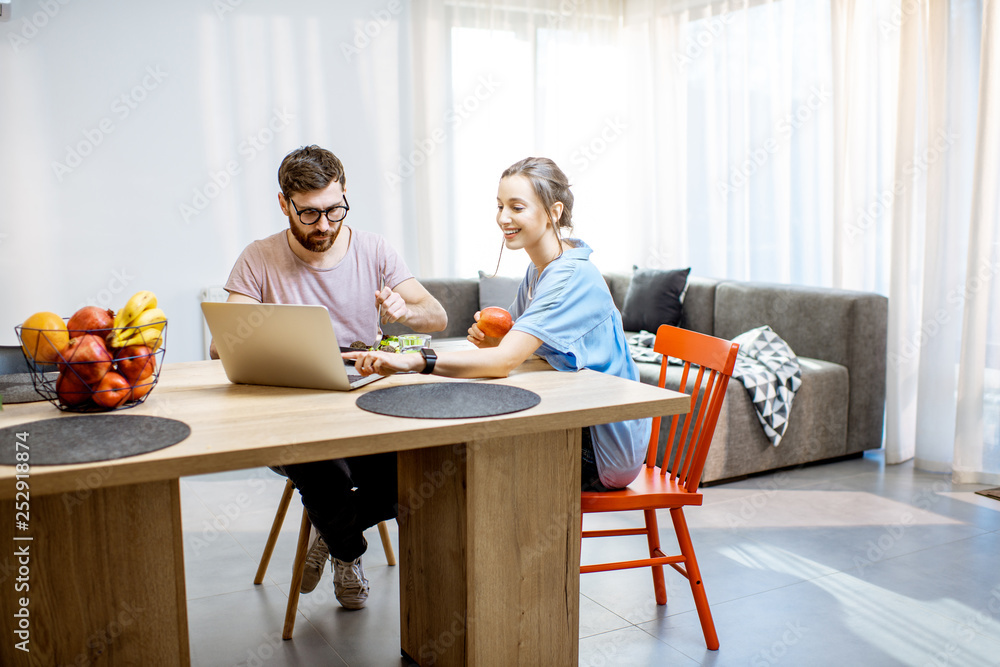 Young couple using laptop during the dinning time with healthy salad in the living room of the moder