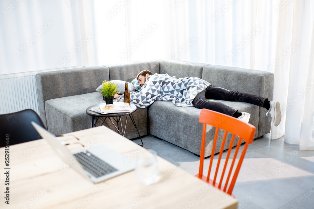 Drunk man lying on the couch covered with blanket, suffering from the alcoholism at home