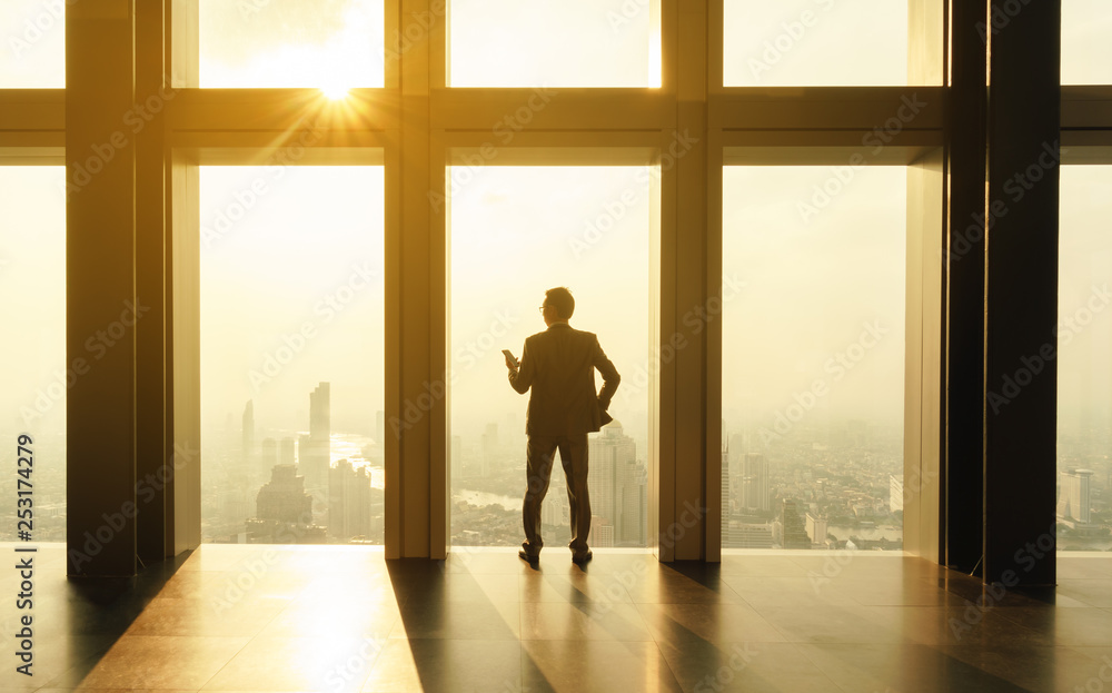 Business man stand by glass window in tall building with background of city