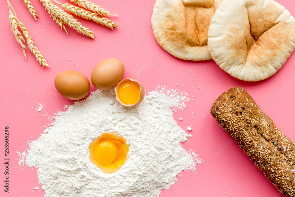 Ingredients for homemade bread. Bread near wheat ears, flour and eggs on pink background top view