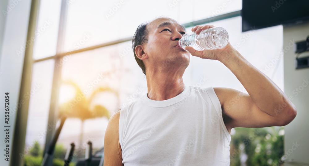 老年人运动后在健身房健身中心喝矿泉水。老年人健康的生活方式。