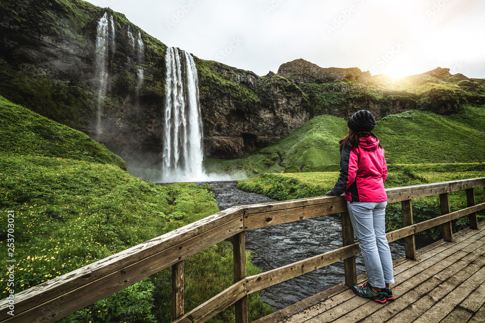 Woman traveler at Magical Seljalandsfoss Waterfall in Iceland located near ring road of South Icelan