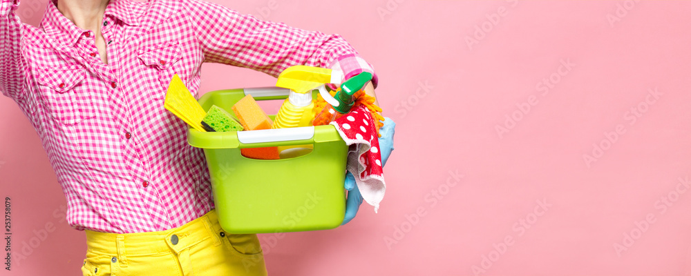 Young woman holding cleaning tools and products in bucket, isolated on white