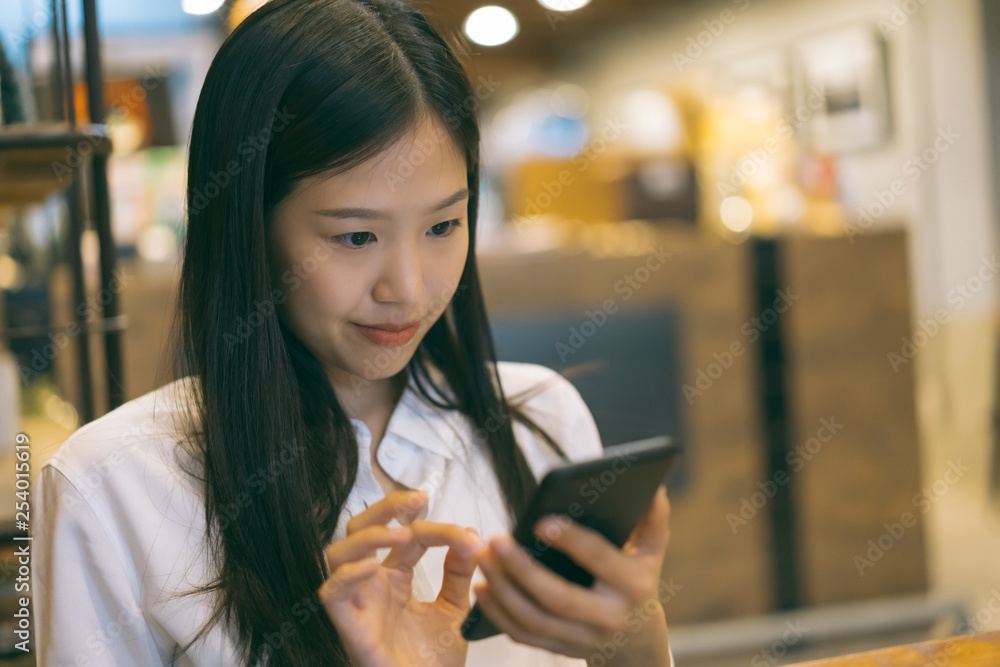 Young Asian woman using phone at a coffee shop happy and smile.