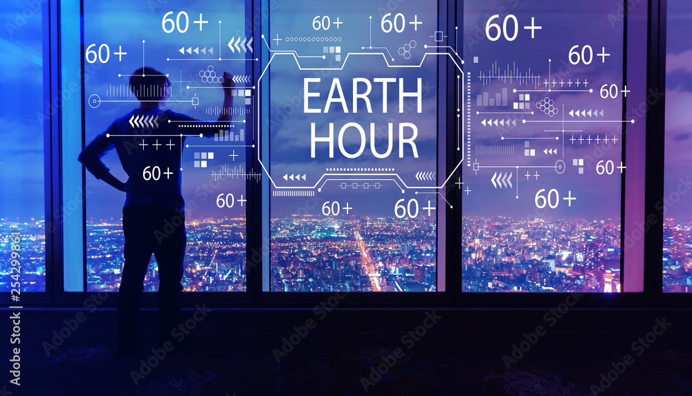 Earth hour with man writing on large windows high above a sprawling city at night