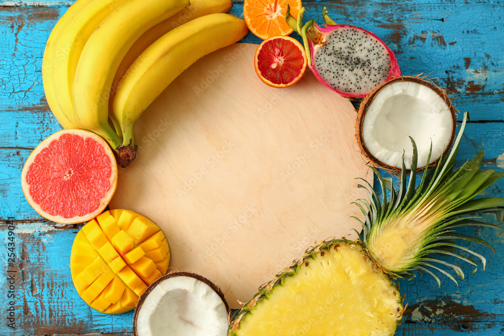 Board with assortment of tropical fruits on color wooden background