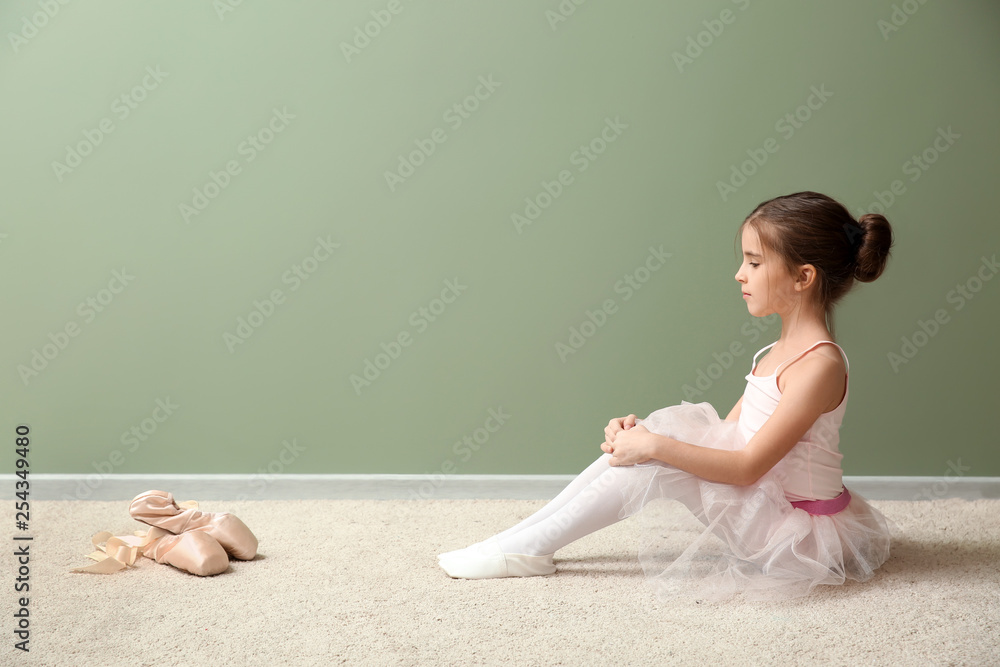 Cute little ballerina sitting near color wall