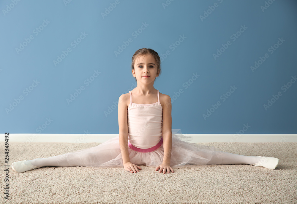 Cute little ballerina stretching near color wall