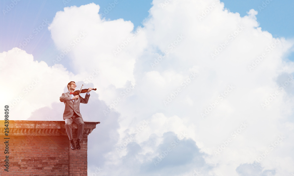 Handsome violinist in glasses on building edge play his melody