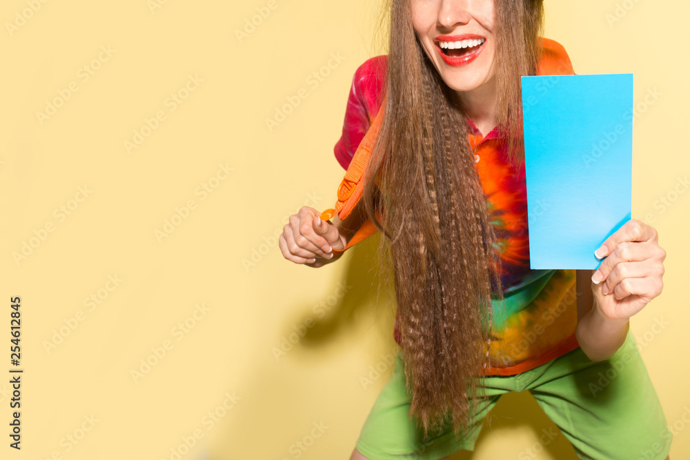 Happy woman with blank card wearing bright clothes and backpack