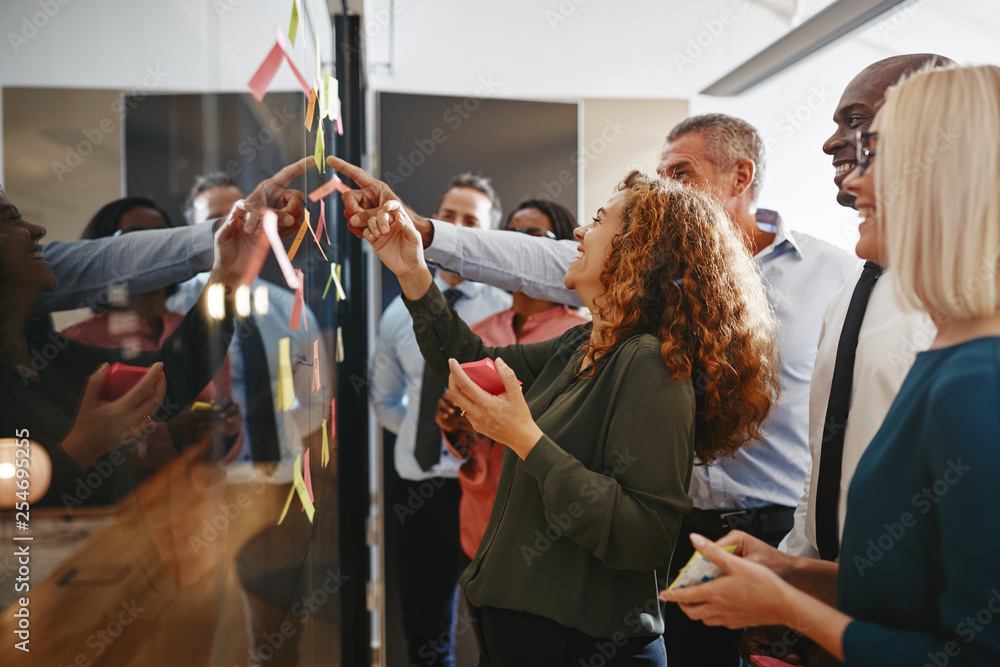 Laughing businesspeople brainstorming with sticky notes on a gla