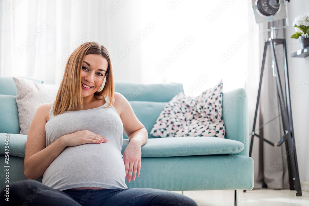 Beautiful smiling pregnant woman sitting on floor at home, looking at camera