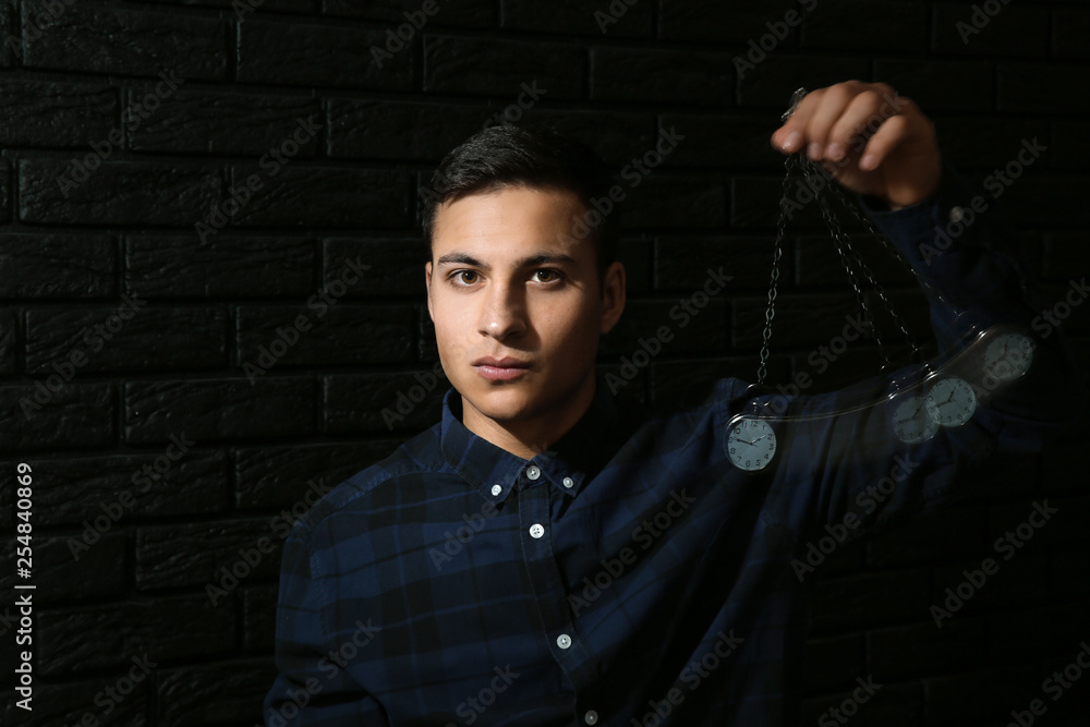 Male hypnotist with swinging pendulum on dark background