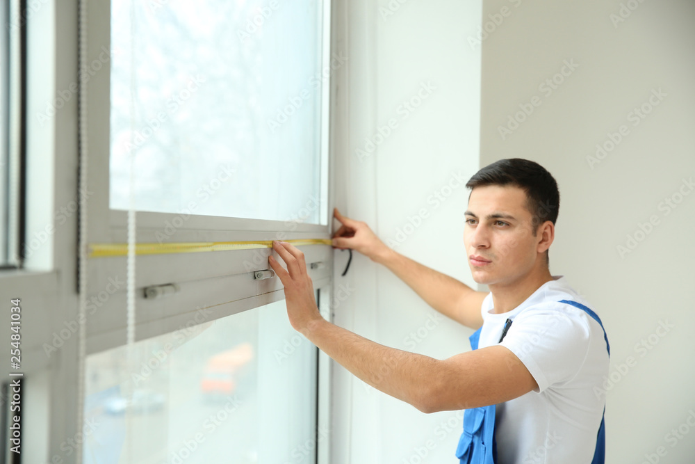 Young worker taking measurements of window in flat