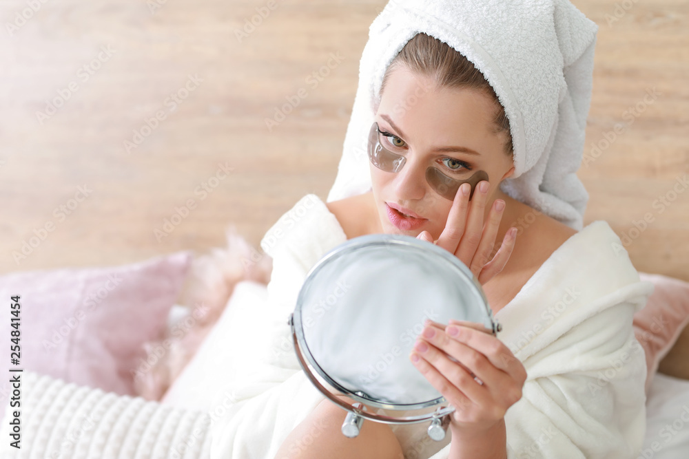 Young woman with under-eye patches looking in mirror at home