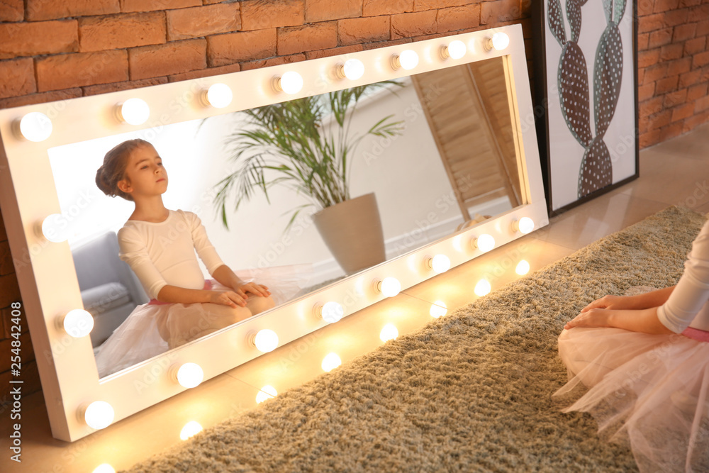 Cute little ballerina sitting in front of mirror at home