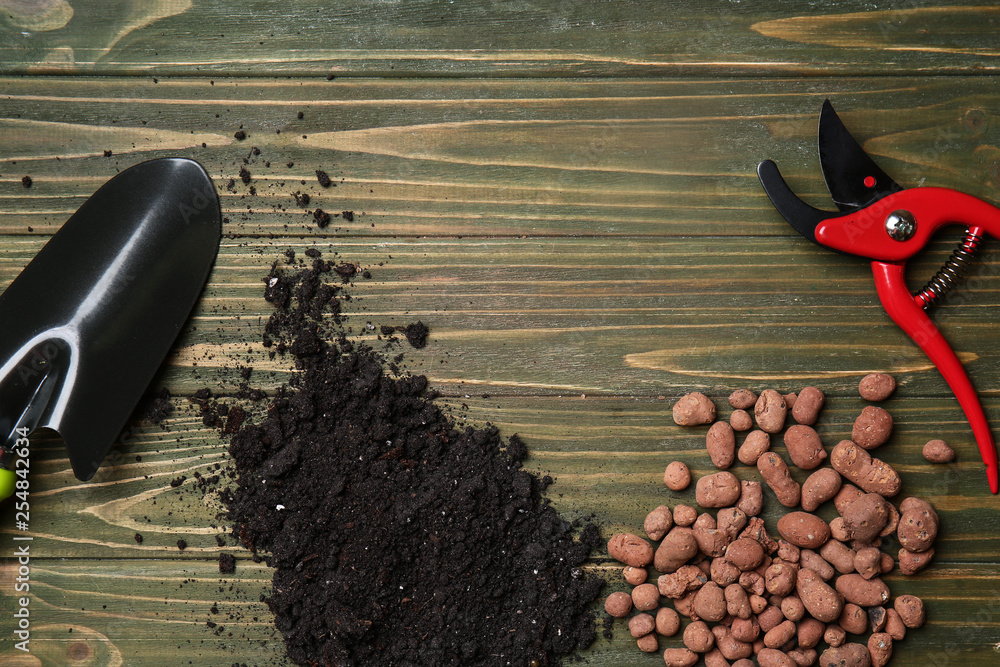 Composition with gardening tools and soil on wooden background