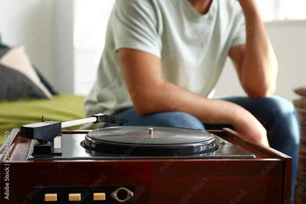 Young man listening to music on record player at home