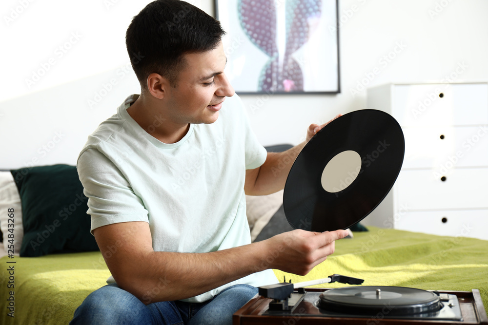 Young man listening to music on record player at home