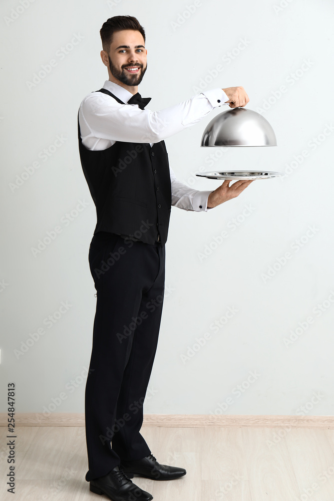 Waiter with tray and cloche near light wall