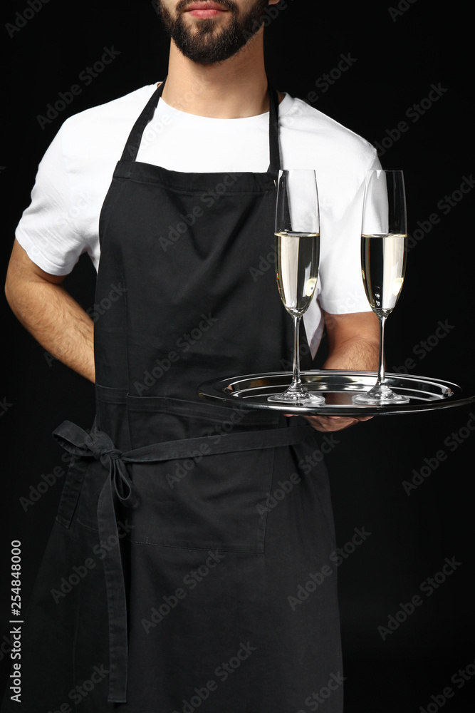 Handsome waiter with glasses of champagne on dark background