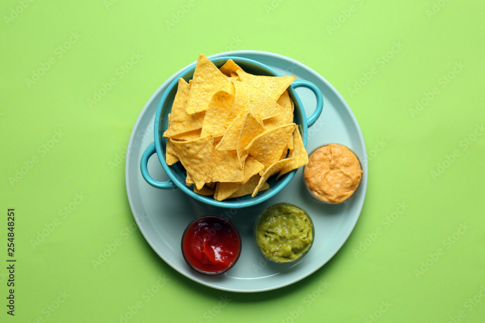 Tasty nachos and sauces on color background