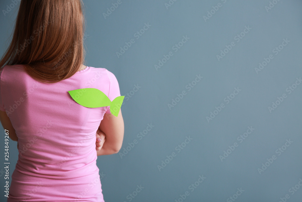 Woman with paper fish on her back against color background. April fools day prank