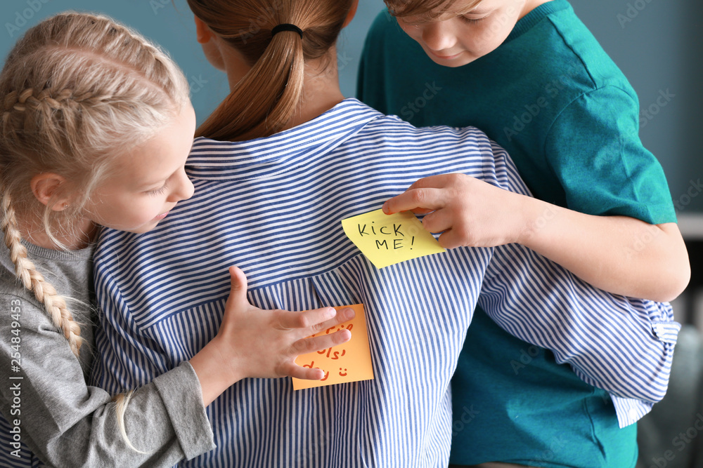 Children attaching paper sheets with text KICK ME and APRIL FOOLS DAY to their mothers back