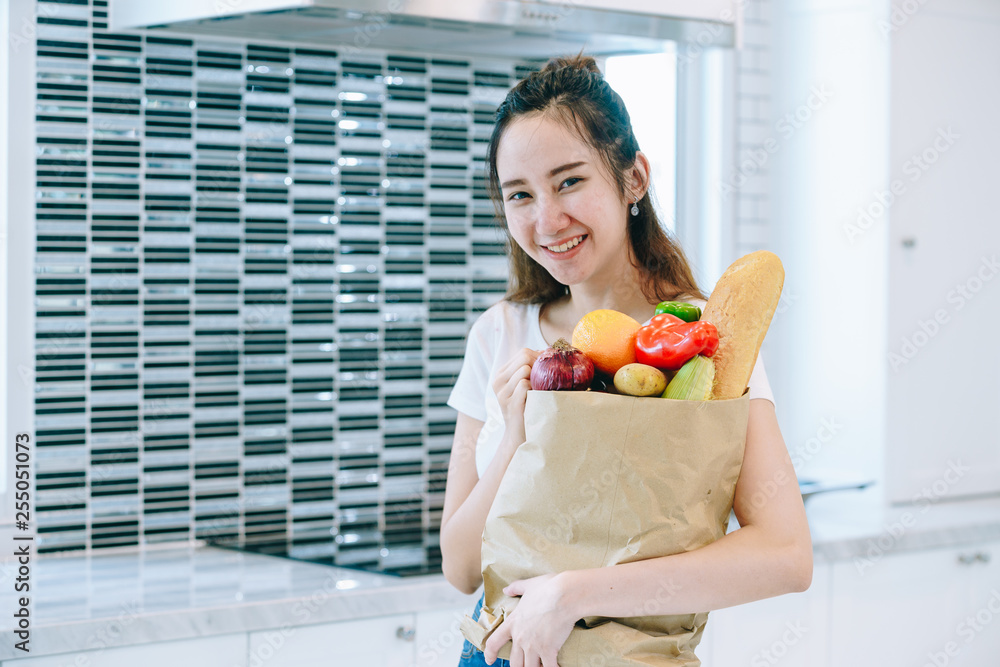 一位亚洲女士在她甜蜜的家里，把水果装在纸袋里放在厨房里做晚饭。