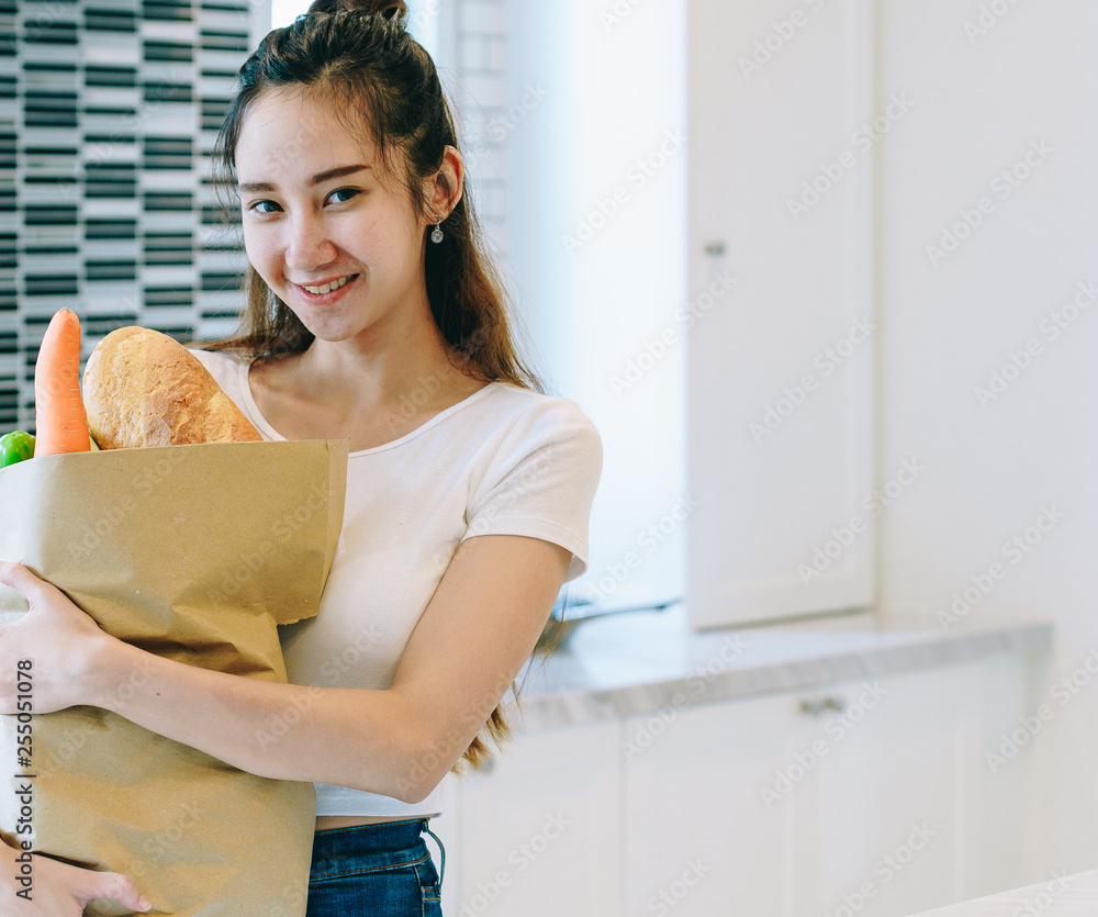 Asian woman holding the fruits in paper bag in her kitchen at her sweet home to making the dinner.