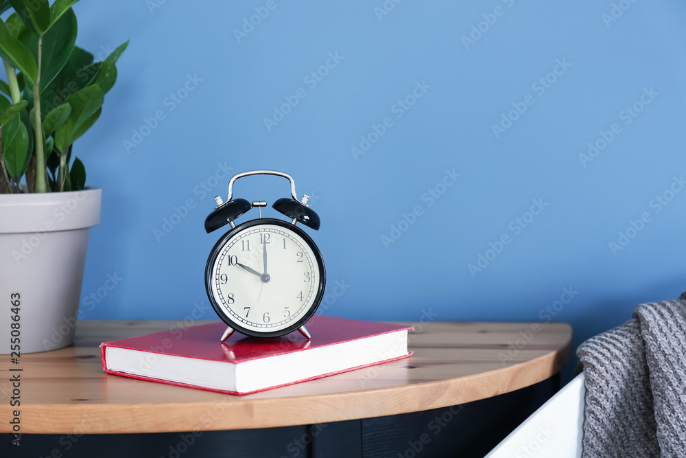 Alarm clock and book on table near color wall