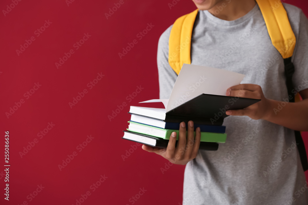 African-American schoolboy with books on color background