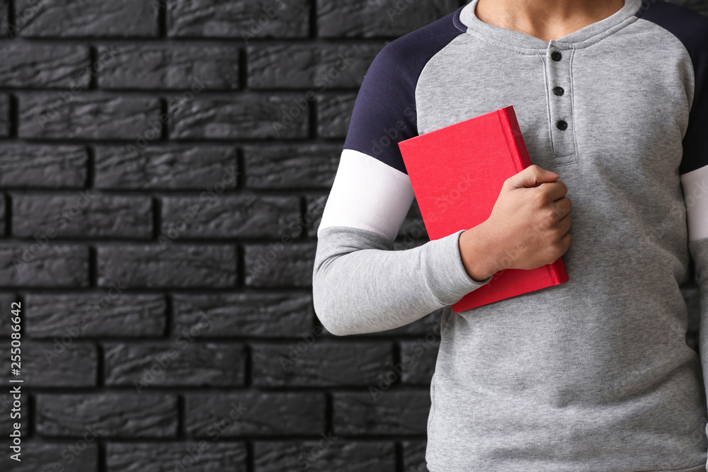 African-American schoolboy with book on dark background