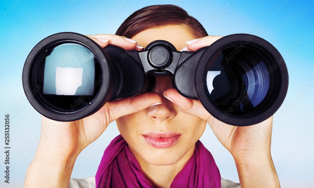 Girl looking into binoculars on light background